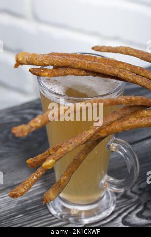 Salsicce sottili per birra. Nelle vicinanze si trova un bicchiere di birra di grano. Sfondo da tavole di pino. Primo piano. Foto Stock