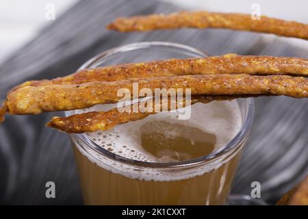 Salsicce sottili per birra. Nelle vicinanze si trova un bicchiere di birra di grano. Sfondo da tavole di pino. Primo piano. Foto Stock