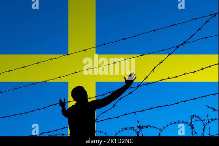 Uomo con braccia tese dietro recinzione spinato con bandiera di Svezia sullo sfondo. Immigrazione, richiedente asilo... concetto Foto Stock