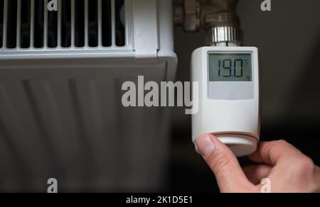 La mano abbassa la temperatura a 19 gradi Celsius su un termostato elettronico. Simbolo per il risparmio energetico. Foto Stock