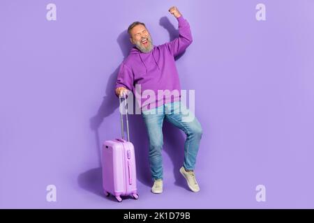 Foto a grandezza naturale di bell'uomo soddisfatto senior vestito viola felpa jeans gridare yeah pugno isolato su sfondo di colore viola Foto Stock