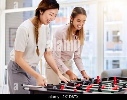 Le donne di affari che giocano il calcio del tavolo, ridendo ed avendo divertimento dell'ufficio al loro lavoro corporativo. Colleghi femmina diversi che si legano mentre competono in un Foto Stock