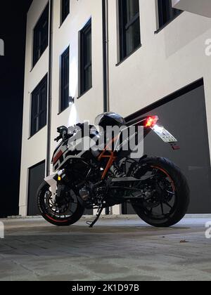 Un primo piano verticale di un duca KTM 125 con ambientazione in bianco e nero di notte vicino ad un edificio Foto Stock