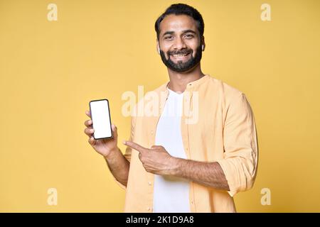 Uomo indiano felice che indica il telefono cellulare isolato su sfondo giallo. Foto Stock
