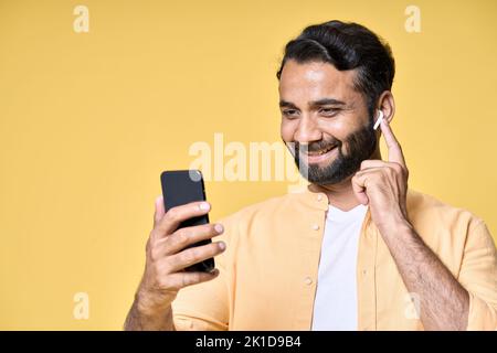 Felice uomo indiano che indossa gli auricolari utilizzando il telefono cellulare effettuare videochiamate. Foto Stock