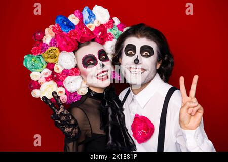 Foto di pauroso scricchioloso coppia uomo signora coccole spettacolo v-segno fare messaggio immagine soccoristi viventi indossare abito nero costume di morte fascia in rosa maschera Foto Stock