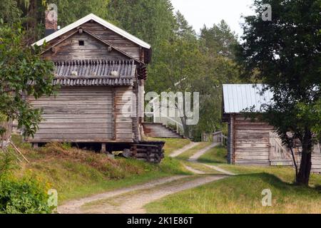 Edifici in legno di legno lungo una strada ghiaiata, sovrastanti. Collina, e un piccolo villaggio sul pendio. Terreno agricolo e foresta sullo sfondo. Foto Stock