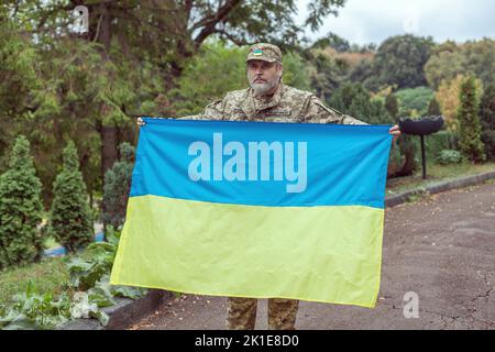 L'uomo militare ucraino tiene la bandiera dell'Ucraina nelle sue mani. Guerra, conflitto, Ucraina. Foto Stock