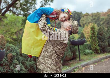 L'esercito ucraino tiene in braccio sua figlia, è avvolto nella bandiera dell'Ucraina. Foto Stock