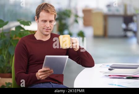 Prendendogli una pausa caffè con un po' di wifi. Un bel uomo d'affari che lavora alla sua scrivania. Foto Stock
