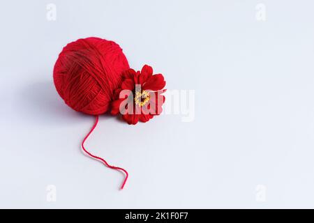 Una palla rossa di filo e un fiore di tsinia su sfondo verde Foto Stock
