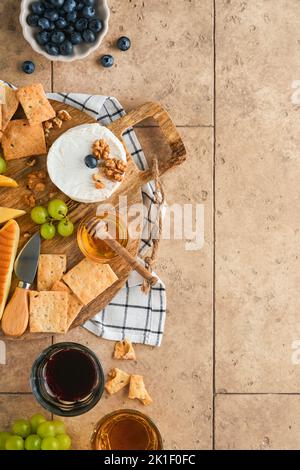 Assortimento di formaggi, miele, cracker, mirtilli, uva con vino rosso e bianco in bicchieri antipasto server su tavola di marmo bianco su fondo grigio Foto Stock