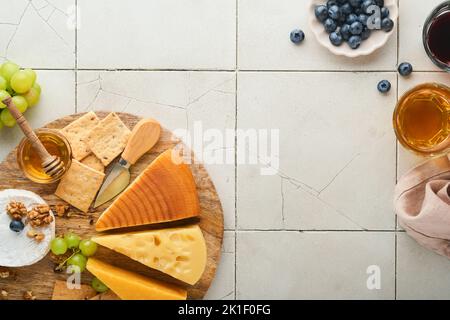 Assortimento di formaggi, miele, cracker, mirtilli, uva con vino rosso e bianco in bicchieri antipasto server su tavola di marmo bianco su fondo grigio Foto Stock