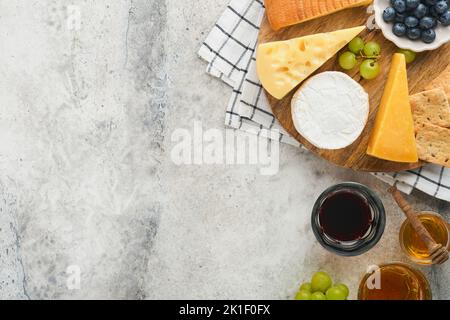 Assortimento di formaggi, miele, cracker, mirtilli, uva con vino rosso e bianco in bicchieri antipasto server su tavola di marmo bianco su fondo grigio Foto Stock