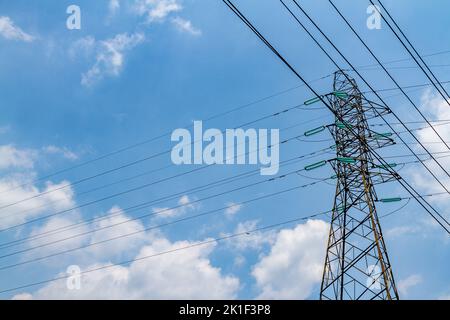 Piloni con struttura in acciaio che supportano linee elettriche ad alta tensione per scopi energetici, fondo cielo blu chiaro con poche nuvole Foto Stock