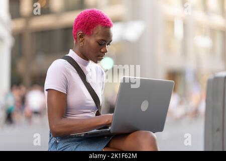 Giovane donna africana che lavora con il portatile per strada Foto Stock