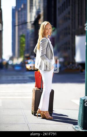 Dite al mondo che siete arrivati. Una bella donna che cammina per una città con i suoi bagagli. Foto Stock