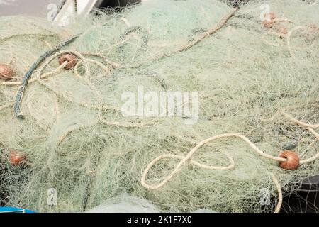 Pile of white fishing nets and green ropes on a fisherman boat in the port area Foto Stock