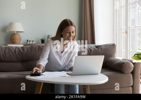 Donna allegra e allegra che utilizza il computer portatile e la calcolatrice Foto Stock