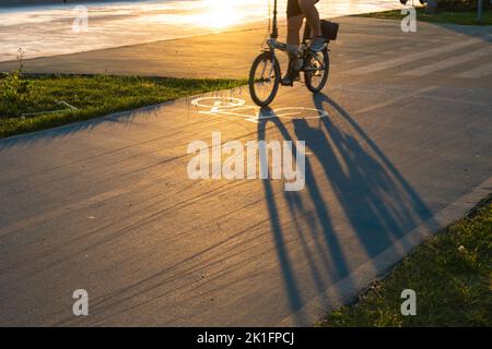 Biker in bicicletta sulla strada ciclabile al tramonto. Ombra del ciclista sulla strada. Concetto di stile di vita sano foto. Messa a fuoco selettiva. Foto Stock