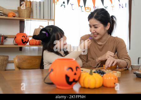 Felice famiglia sorridente madre e figlia facendo Halloween decorazioni in casa insieme, mentre si siede al tavolo di legno. Foto Stock