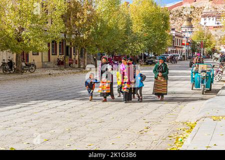 Gruppo di famiglie shopping sulla strada principale di Gyantse Town, Prefettura di Shigatse, Tibet Cina con il monastero buddista Pelkor Chode sullo sfondo Foto Stock