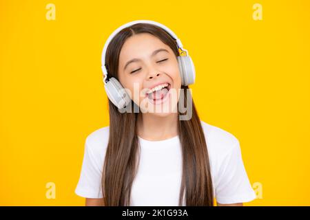 Adolescente in moderne cuffie wireless che ascolta la musica delle canzoni nell'app audio, ascoltando la sua musica preferita su sfondo giallo dello studio. Foto Stock