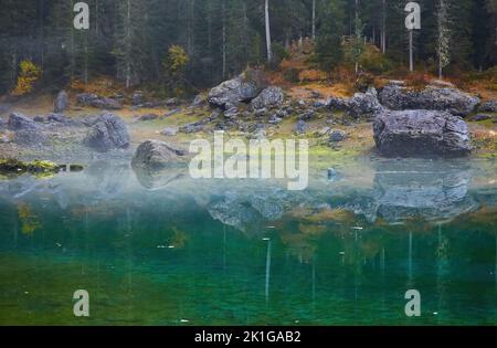 Pietre e alberi si riflettono nel lago di Carezza Karersee , Patrimonio Naturale dell'Umanità dell'UNESCO, Nova Levante, Alto Adige Foto Stock