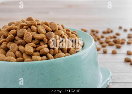 Cibo secco per gatti e cani in una ciotola verde su uno sfondo di legno. Primo piano. Foto Stock