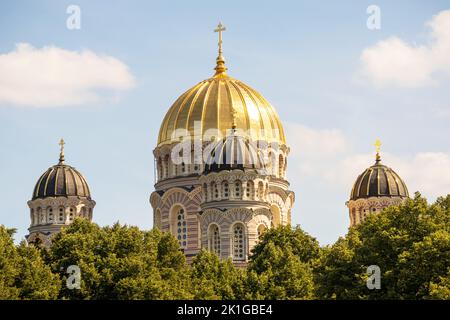 Una chiesa con un muro giallo e una punta dorata appuntita nel centro della città con più finestre e alberi accanto ad essa Foto Stock