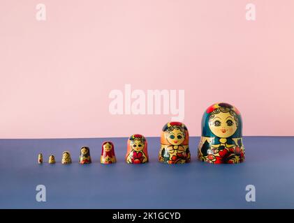 Bambole russe anche note come matryoshka o babushka impilate su uno sfondo rosa e blu. Concetto minimo. Foto Stock