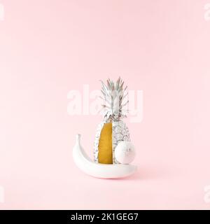 Ananas fresco, banana e limone di colore bianco su sfondo rosa. Concetto di cibo estivo minimo. Foto Stock
