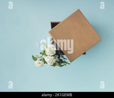 Fiori bianchi in scatola di cartone regalo marrone su sfondo blu. Consegna fiori. Concetto minimo. Foto Stock