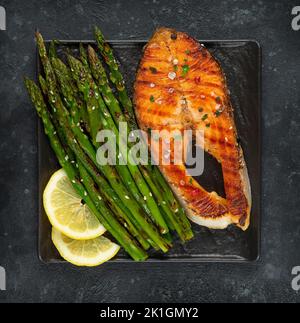 Bistecca di salmone alla griglia e asparagi sulla griglia su fondo scuro. Direttamente sopra Foto Stock