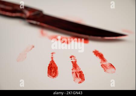 La lama sanguinante e la mano stampano nel sangue su un tavolo bianco. Foto Stock