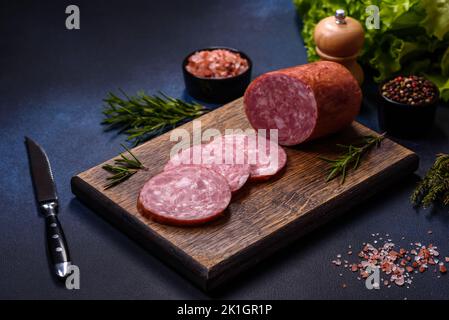 Deliziosa salsiccia affumicata fresca tagliata a fette su un tagliere di legno su uno sfondo di cemento scuro Foto Stock