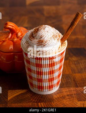 Una zucca Spice latte con panna montata in una tazza monouso su un tavolo di legno Foto Stock