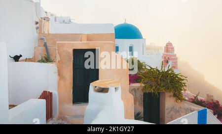 Un gatto nero su una mattina nebbiosa e nebbiosa durante l'alba dell'ora d'oro presso la tradizionale cupola blu della chiesa greco-ortodossa di Agios Nikolaos nel villaggio o Foto Stock