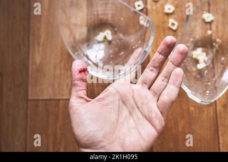 Primo piano di un dito di donna tagliato, sullo sfondo di una tazza spaccata con tagliatelle. Una ferita con sangue ricevuto durante la pulizia dei piatti rotti. Foto di alta qualità Foto Stock