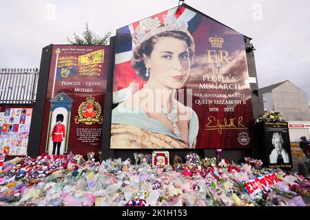 Dopo la scomparsa del Monarca britannico, la gente depone fiori in un murale raffigurante la Regina Elisabetta II sulla Shankill Road a Belfast. Foto Stock