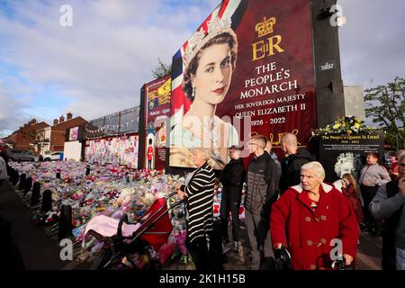 Dopo la scomparsa del Monarca britannico, la gente depone fiori in un murale raffigurante la Regina Elisabetta II sulla Shankill Road a Belfast. Foto Stock