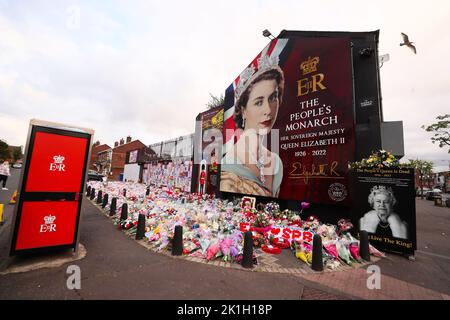 Dopo la scomparsa del Monarca britannico, la gente depone fiori in un murale raffigurante la Regina Elisabetta II sulla Shankill Road a Belfast. Foto Stock