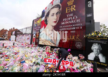 Dopo la scomparsa del Monarca britannico, la gente depone fiori in un murale raffigurante la Regina Elisabetta II sulla Shankill Road a Belfast. Foto Stock