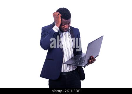 giovane uomo d'affari dimenticato che indossa un abito elegante e tiene il portatile mentre graffia la testa con la mano. Foto Stock