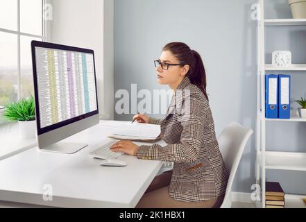 Il financier femminile concentrato calcola gli account interni dell'azienda utilizzando un foglio di calcolo Excel. Foto Stock