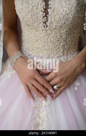 Splendida sposa, che indossa un esclusivo abito in tulle rosa o lilla impreziosito da perle e perle sulla parte superiore e tiene le mani davanti Foto Stock