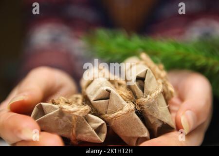 Primo piano le mani femminili con tre piccoli regali artigianali. Giovane donna hipster in maglione di Natale che tiene 3 regali organici, arco di corda. Accogliente inverno caldo de Foto Stock