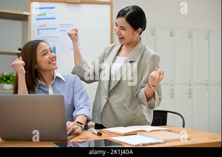 Due donne d'affari asiatiche, felici e allegre, festeggiano il successo dei loro progetti in ufficio. Ricevendo buone notizie, vincendo i progetti. Foto Stock
