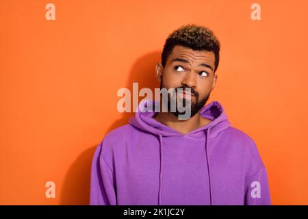 Foto di misterioso ragazzo vestito viola abiti pullover guardare spazio vuoto isolato su sfondo di colore arancione Foto Stock