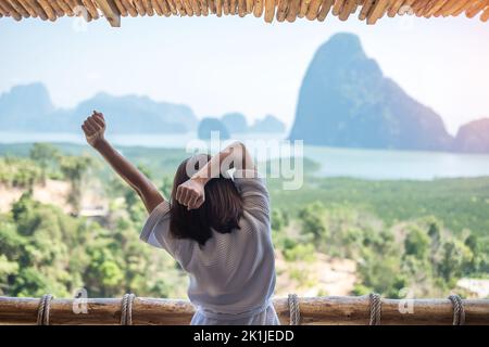 Donna felice in accappatoio stretching dopo il risveglio e godere del punto di vista della baia di Phang Nga, turista rilassante in resort tropicale a Samet Nang She, vicino a Phu Foto Stock